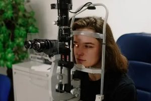 A woman undergoing an eye exam, using a phoropter machine as the optometrist adjusts the lenses