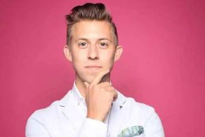 Professional man in a white lab coat with a thoughtful expression against a pink background.